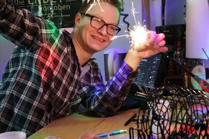Kevin hält zwei brennende Wunderkerzen während der Silvesterfeier, es gibt buntes Licht und auf einem Tisch steht ein Bingo-Spiel.